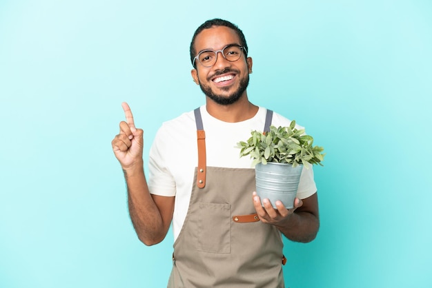 Tuinman Latijns-man met een plant geïsoleerd op een blauwe achtergrond die een vinger toont en optilt in teken van het beste