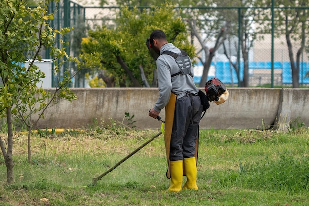 Tuinman maait gras met gemotoriseerde zeis in de tuin