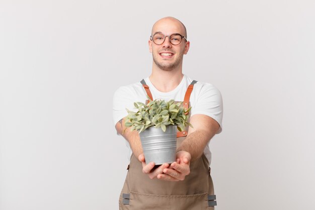 Tuinman man glimlachend gelukkig met vriendelijke, zelfverzekerde, positieve blik, aanbieden en tonen van een object of concept