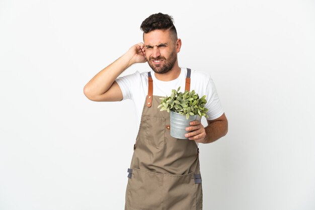 Tuinman man met een plant over geïsoleerde witte muur gefrustreerd en oren bedekken