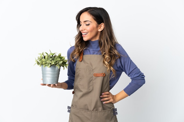 Tuinman meisje met een plant geïsoleerd op een witte achtergrond poseren met armen op heup en glimlachen