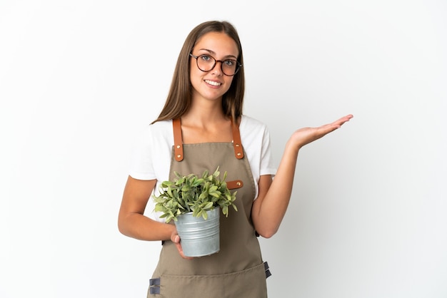 Tuinman meisje met een plant over geïsoleerde witte achtergrond handen uitbreiden naar de zijkant voor uitnodigend om te komen