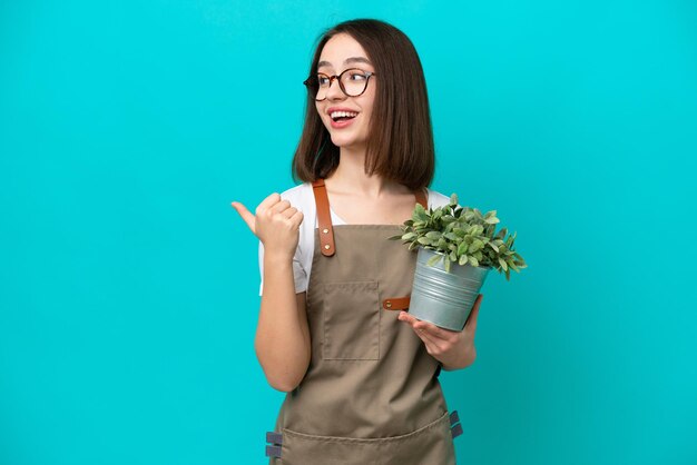 Tuinman Oekraïense vrouw met een plant geïsoleerd op een blauwe achtergrond, wijzend naar de zijkant om een product te presenteren