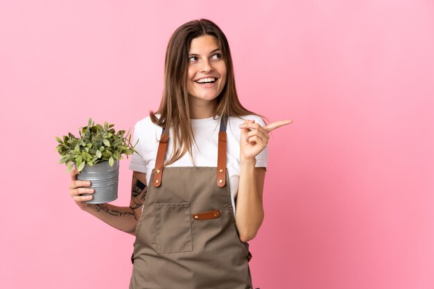 Tuinman vrouw met een plant geïsoleerd op roze van plan om de oplossing te realiseren terwijl ze een vinger opheft