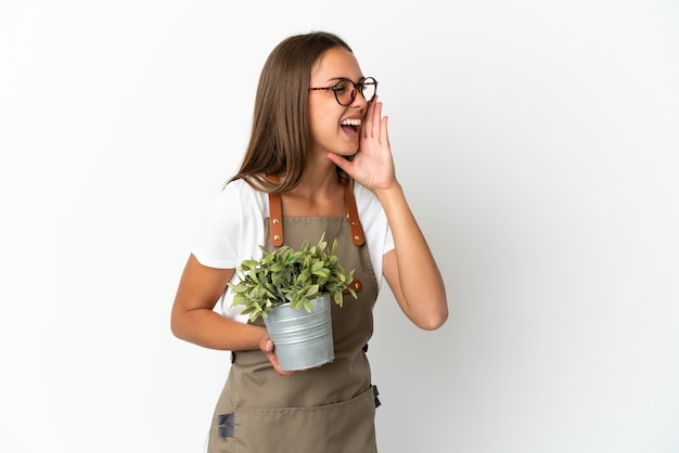 Tuinmanmeisje dat een plant over een geïsoleerde witte achtergrond vasthoudt en met wijd open mond naar de zijkant schreeuwt