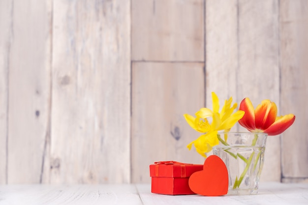 Tulip flower arrangement in glass vase with heart greeting, watering can decor on wooden table background wall, close up, Mother's Day design concept.