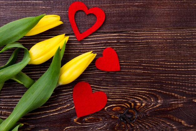 Tulips and hearts on wood. Yellow flowers near fabric hearts. Tender flowers for wife. Spring holiday festive mood.