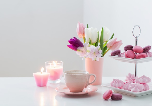 Tulips in vase and cup of coffee with dessert on white