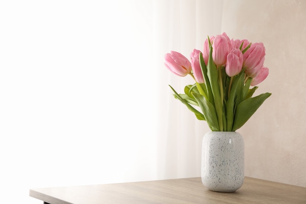 Tulips in vase on wooden background, space for text