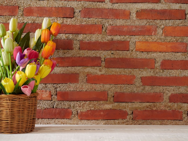 Tulpen in mand op witte tafel tegen bakstenen muur