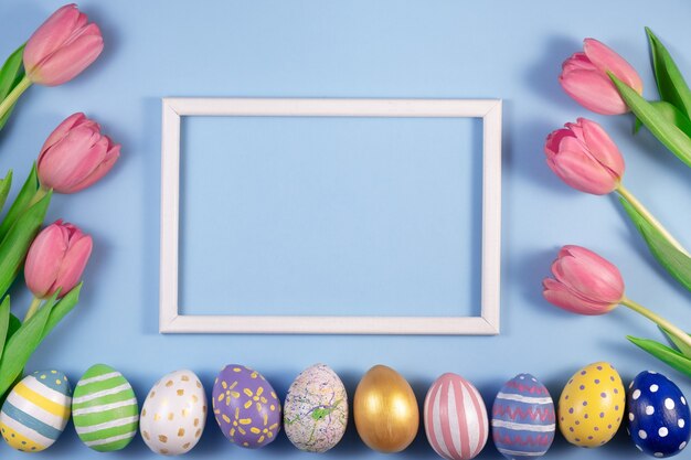 Tulpenbloemen en paaseieren met houten frame dat op blauw wordt geïsoleerd