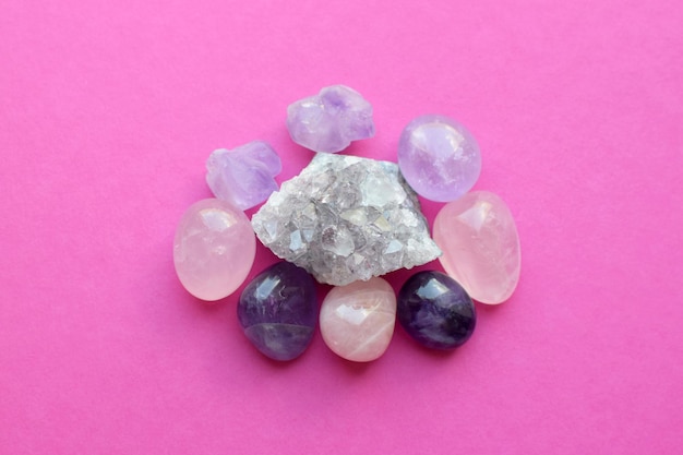 Tumbled gems of various colors amethyst and rose quartz on pink\
background