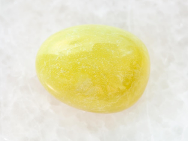 Tumbled yellow calcite gemstone on white marble