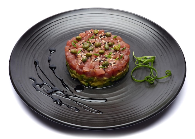 Tuna and avocado tartare with sesame seeds and capers on a dark ceramic plate
