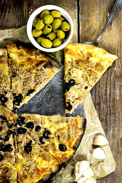 tuna pizza with cheese and tomato and olives and garlic on wood table