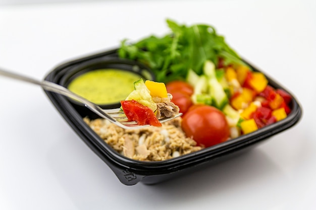 Tuna salad on a fork, black salad container