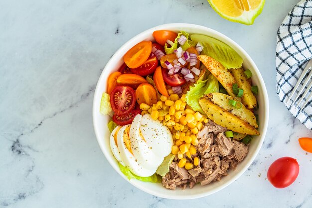 Foto insalata di tonno con uova, verdure e mais in una ciotola bianca sullo sfondo bianco