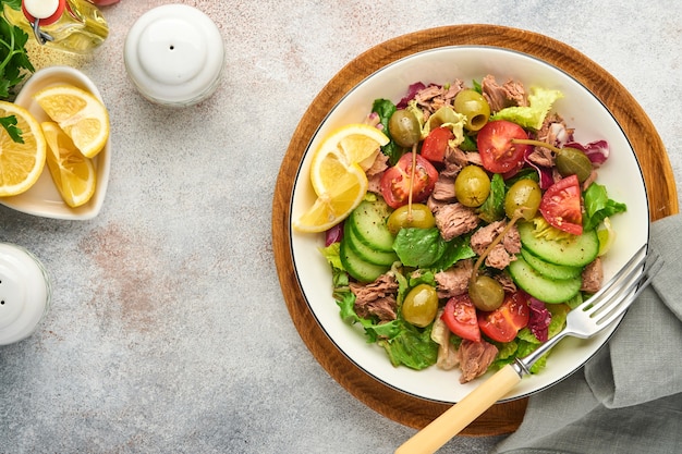 Tuna salad with fresh vegetables, olives, capers and lemon served in bowl on light grey background. Top view with copy space.