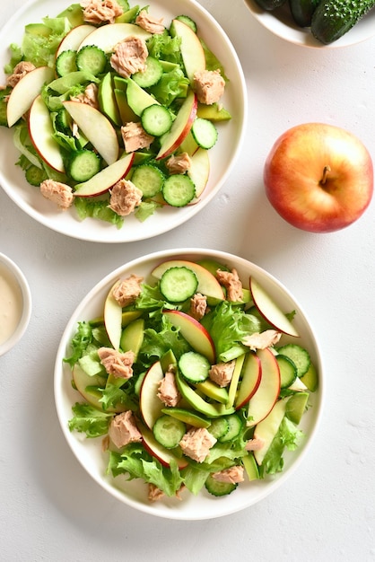 Tuna salad with slices of cucumber avocado red apple in bowl over white stone background Top view