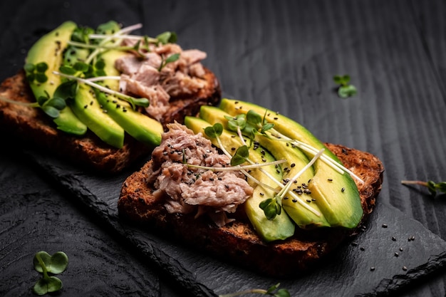 Tuna sandwiches with avocado and microgreen on wholemeal bread wooden background Tasty tuna sandwiches for breakfast Healthy snack Top view flat lay