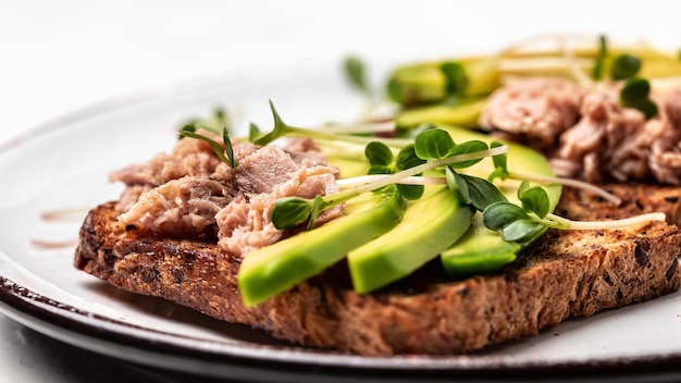 Tuna sandwiches with avocado and microgreen on wholemeal bread wooden background Tasty tuna sandwiches for breakfast or snack Top view flat lay copy space