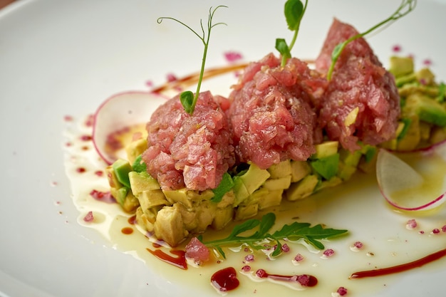 Tuna tartare with avocado and sauce in a white plate on a wooden background