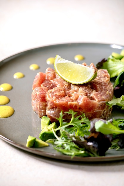 Tuna tartare with green salad, lime, avocado and mustard sauce serving on ceramic plate . Fine dining, restaurant appetizer