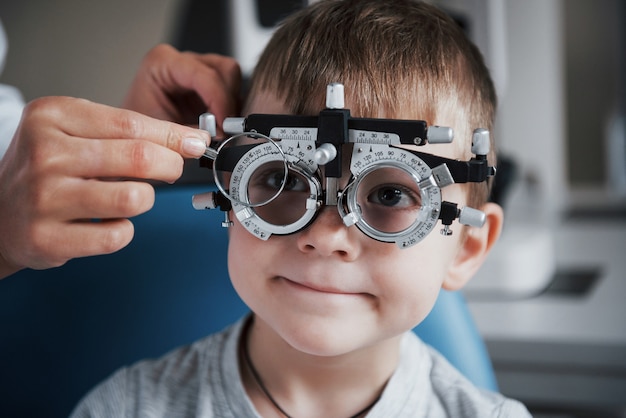 Tuning the intrument. Little boy with phoropter having testing his eyes in the doctor's office.