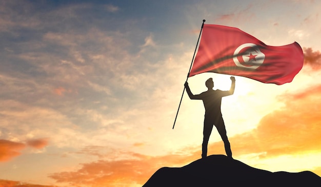 Tunisia flag being waved by a man celebrating success at the top of a mountain 3D Rendering