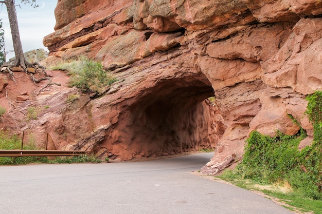 Tunnel in a red rock formation through which a sphalted road goes through