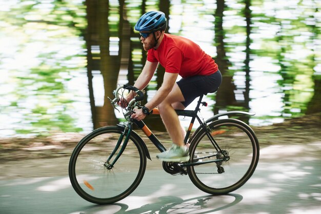 Turing to the left. Cyclist on a bike is on the asphalt road in the forest at sunny day