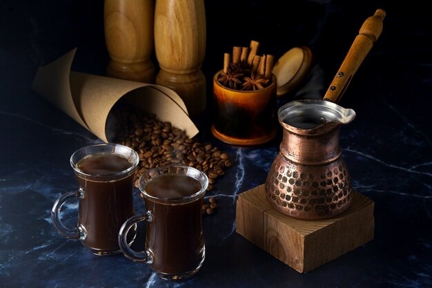 Turk and two cups of hot coffee with spices and coffee beans on
a dark background