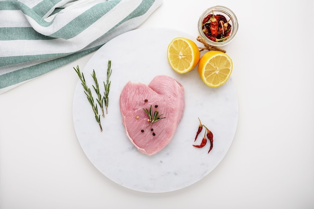 Turkey, chicken fillet on white marble Board with spices, lemon, chili pepper, rosemary on white background, top view, meat concept