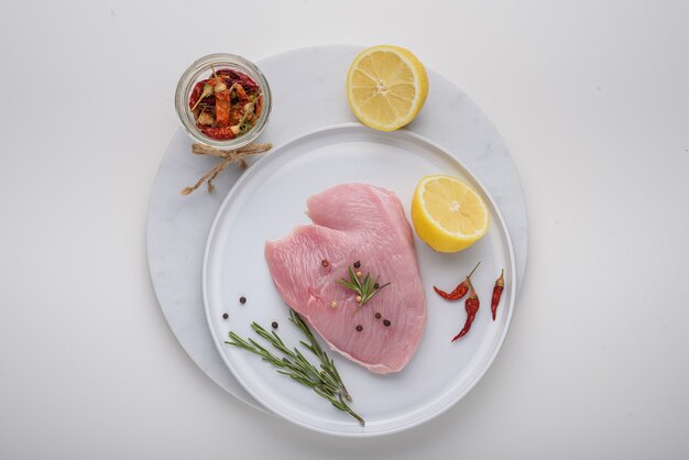 Turkey, chicken fillet on white marble Board with spices, lemon, chili pepper, rosemary on white