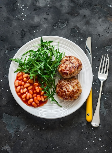 Turkey cutlets beans tomato sauce and arugula salad on a dark background top view Delicious healthy lunch