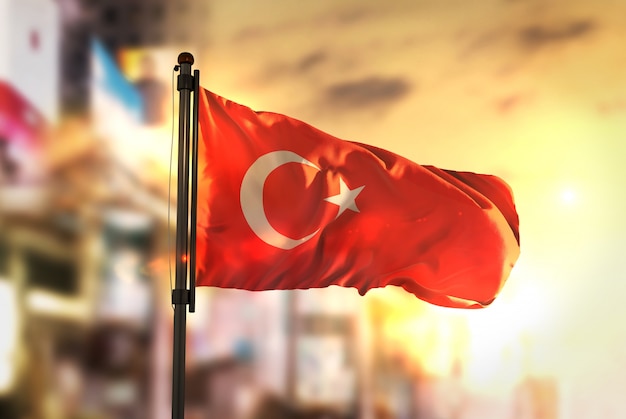 Turkey Flag Against City Blurred Background At Sunrise Backlight