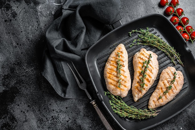 Turkey grilled breast fillet steaks in a frying pan. Black background. Top view. Copy space.