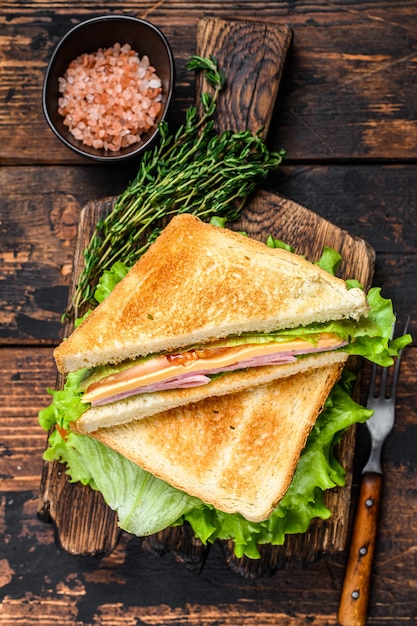 Turkey Ham Club sandwiches with cheese, tomatoes and lettuce on a wooden cutting board. Dark  wooden table. Top view.