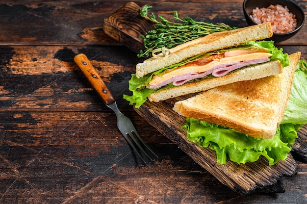 Turkey ham club sandwiches with cheese, tomatoes and lettuce on a wooden cutting board