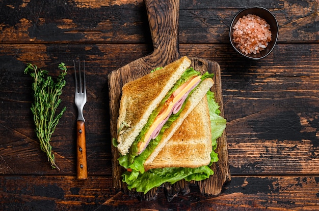 Turkey Ham Club sandwiches with cheese, tomatoes and lettuce on a wooden cutting board