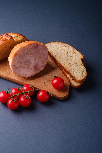 Turkey ham meat, fresh cherry tomatoes branch and loaf sliced bread on wooden cutting board