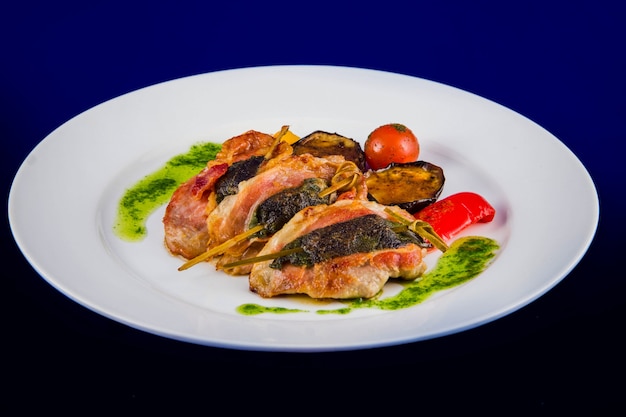 터키 메달리온은 구운 야채와 파란색 배경에 흰색 접시에 페스토 소스 꼬치에 허브와 박제.