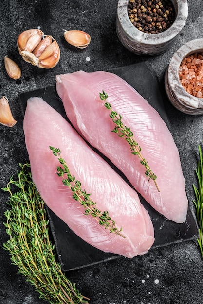 Turkey raw breast fillet steaks on marble board with herbs. Black background. Top view.