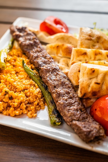 Kebab turco adana su un piatto con peperoni marinati, pane e riso pilaf. vista dall'alto.