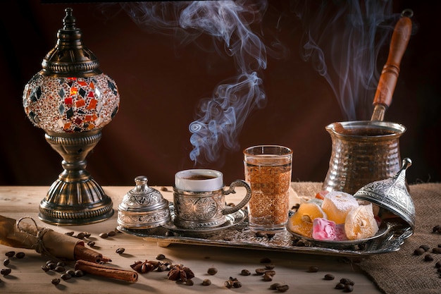 Turkish coffee in cezve and traditional Turkish delight. Steam over a cup. Antique lamp