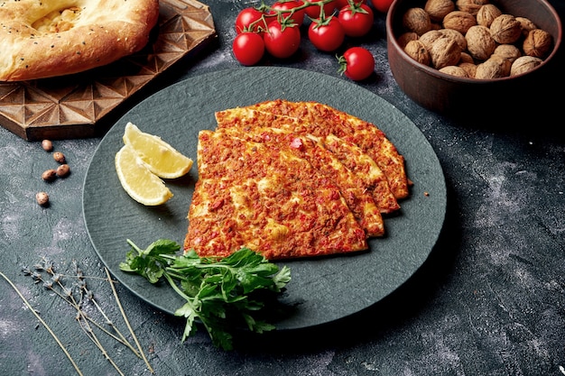 Turkish cuisine dish - pide with minced meat and tomatoes on a black plate. Turkish lahmajun, close up,