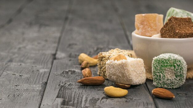 Turkish delight and nuts in a white cup on a wooden table. Oriental sweets. Space for the text.