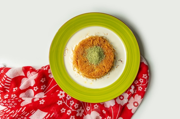 Турецкий десерт кунефе кунафа кадайиф с фисташками с порошком грецкого ореха в блюде, изолированном на красочной скатерти, вид сверху на сером фоне
