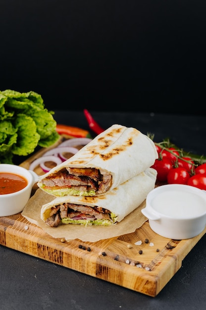 Turkish doner kebab on lavash with beef fresh salad and vegetables lying on board with sauces