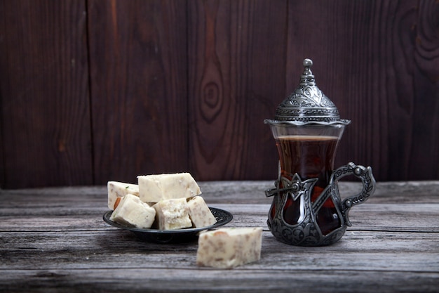 Turkish glass with tea and halva on a metal plate stand on a wooden background.